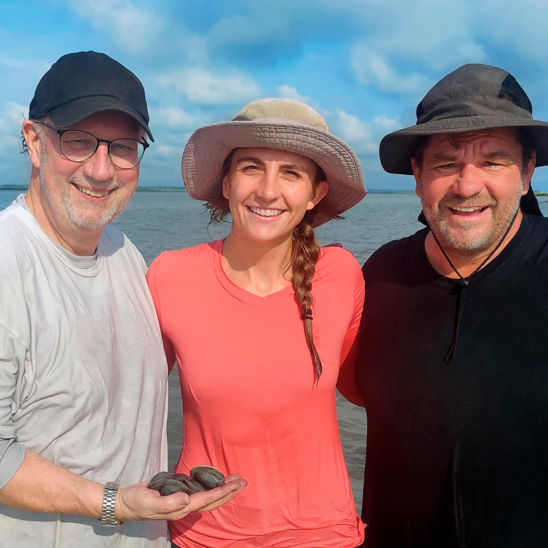Steve Schrock, Sydney West and Joe Williams on the shore holding clams